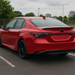 Red car parked on a road with a cloudy sky in the background and gloss black spoiler