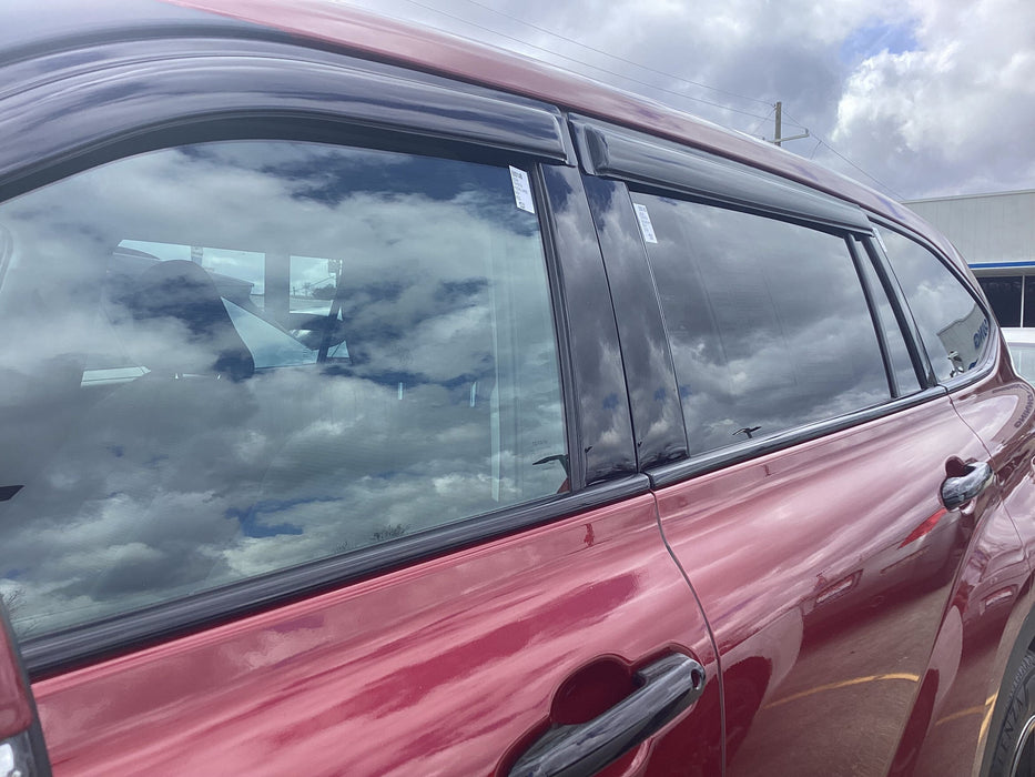 Close-up of a red car's side black window trim with a cloudy sky reflection.